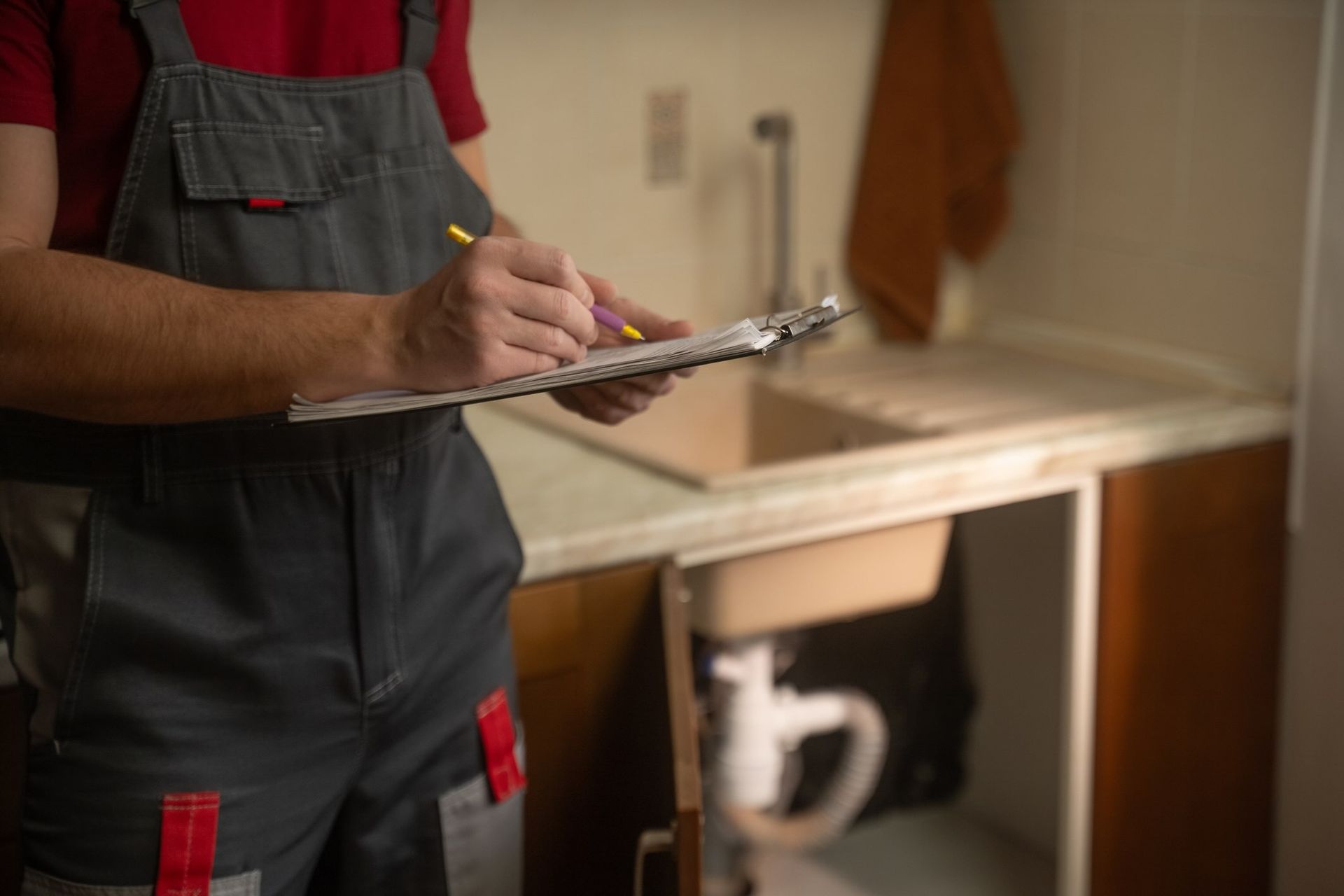 A man wearing a plumber's uniform writes on a clipboard.