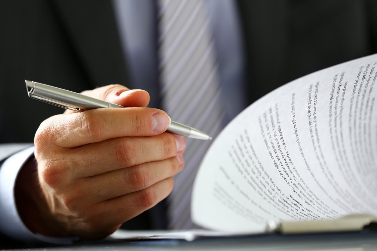 Male arm in suit and tie fill form clipped to pad with silver pen closeup. 