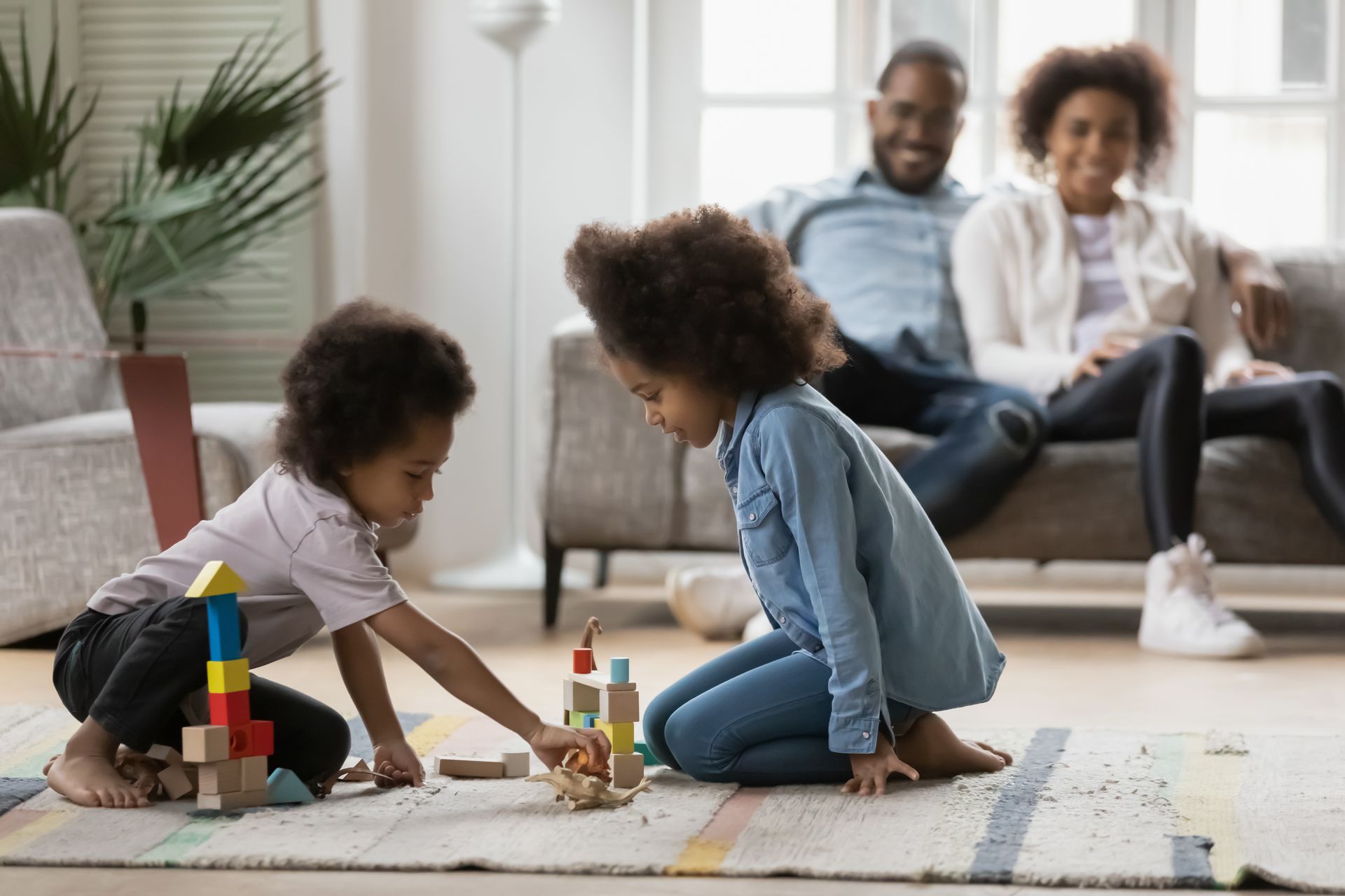 The children play with their parents sitting on the couch in the back discussing the differences between self-insured and fully-insured plans for their family