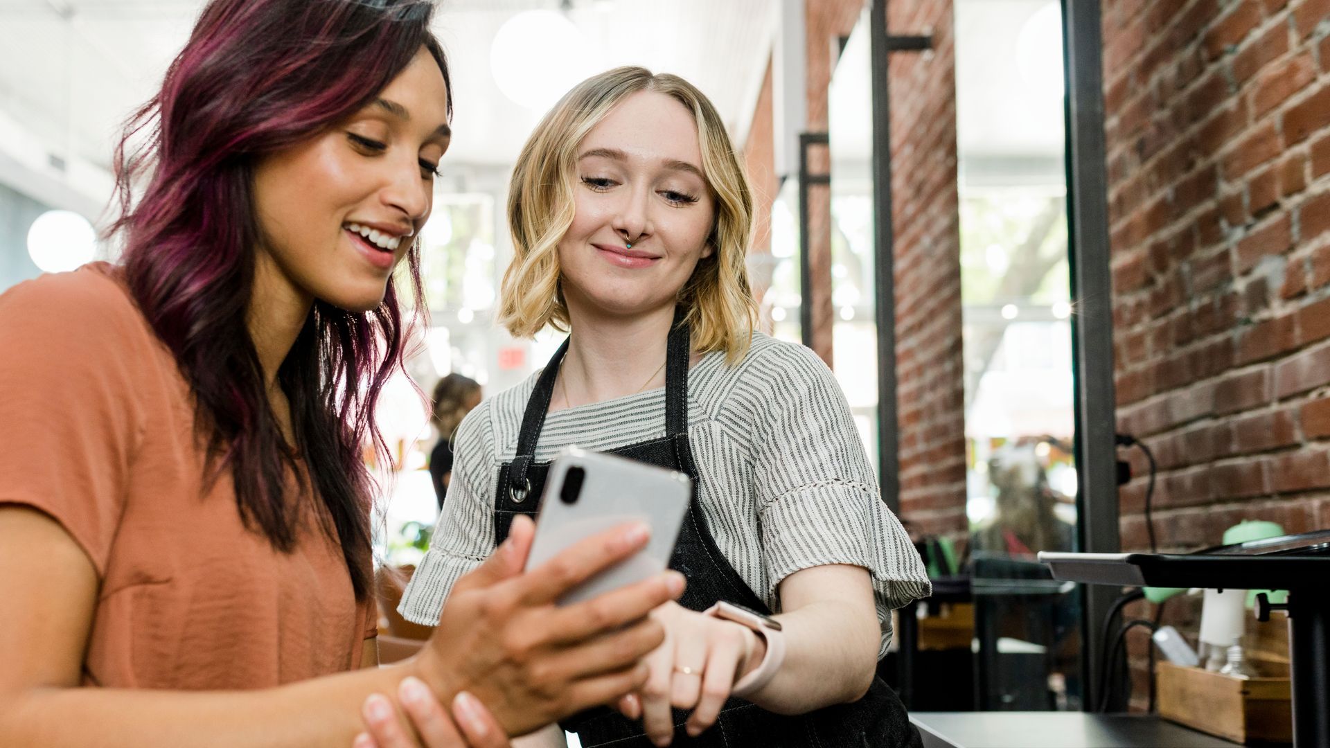 Two women are looking at a cell phone in a salon looking at commercial property insurance options