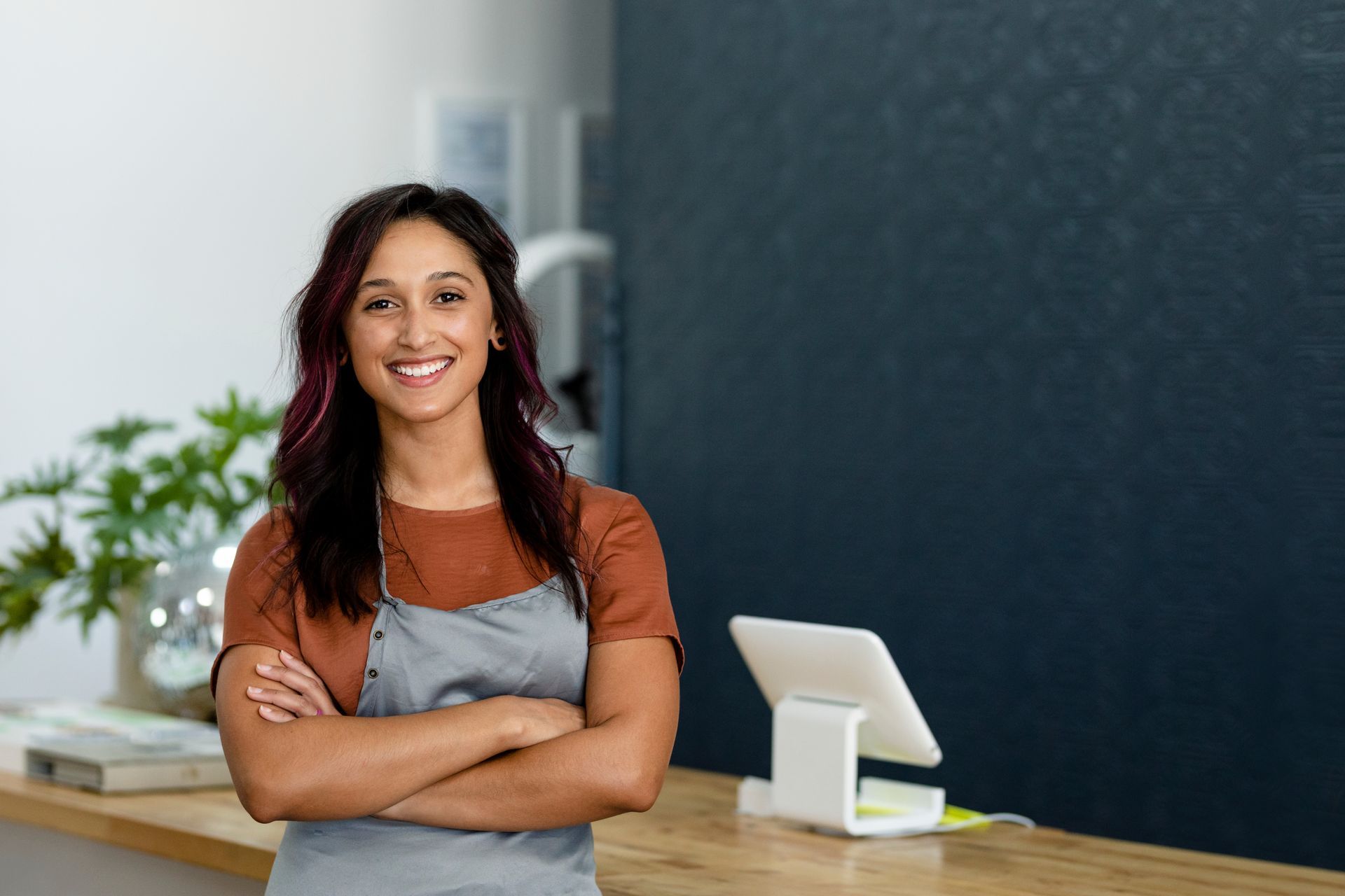 A woman in an apron is standing in front of a counter with her arms crossed -- her salon is protected by commercial property insurance