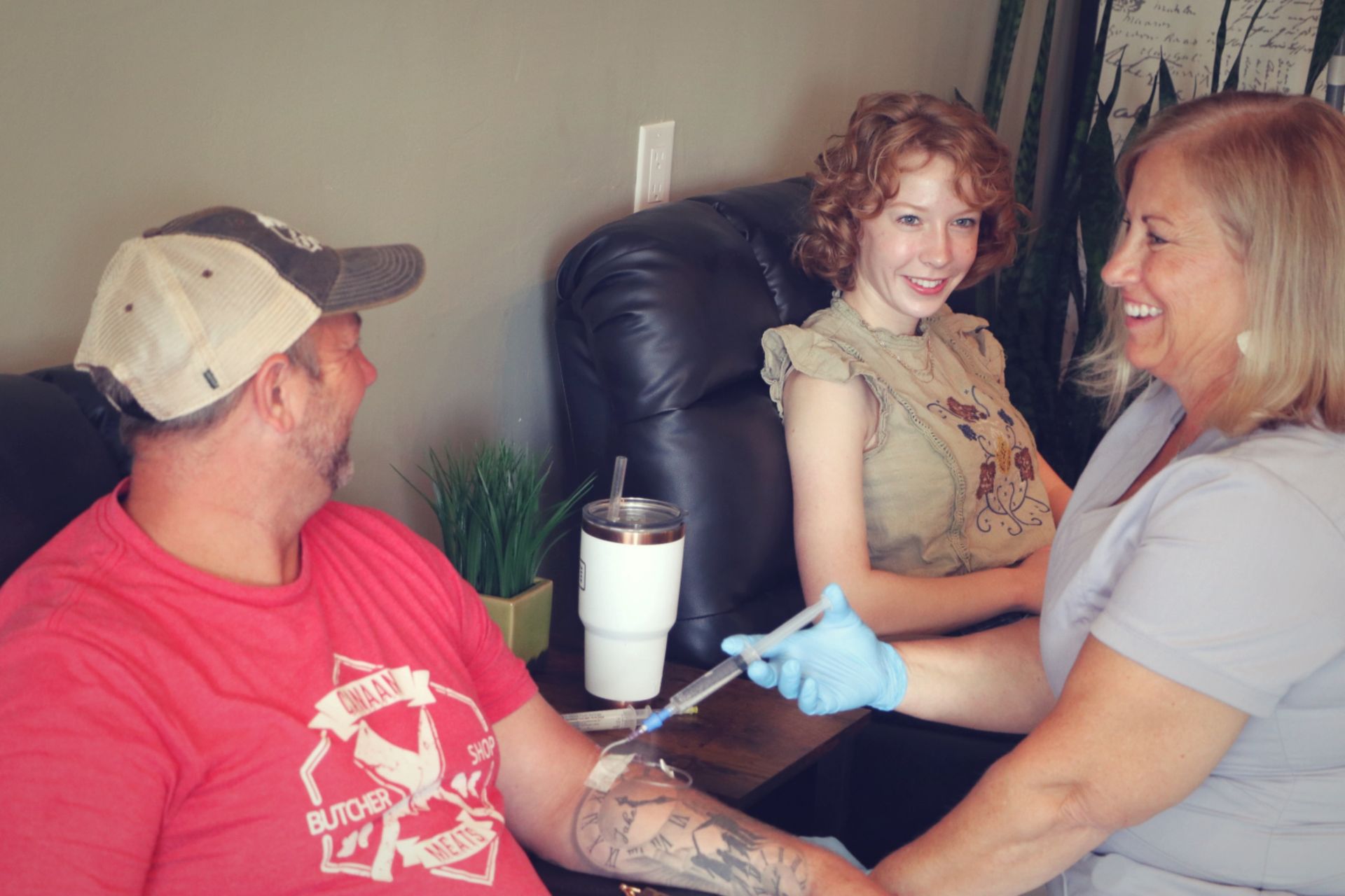 A man and a woman are sitting on a couch while a nurse is giving a glutathione injection.