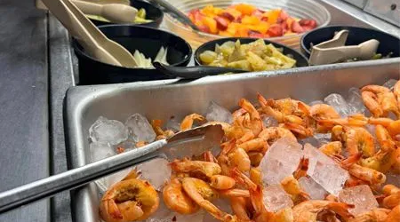 A tray of shrimp on ice with tongs in it.