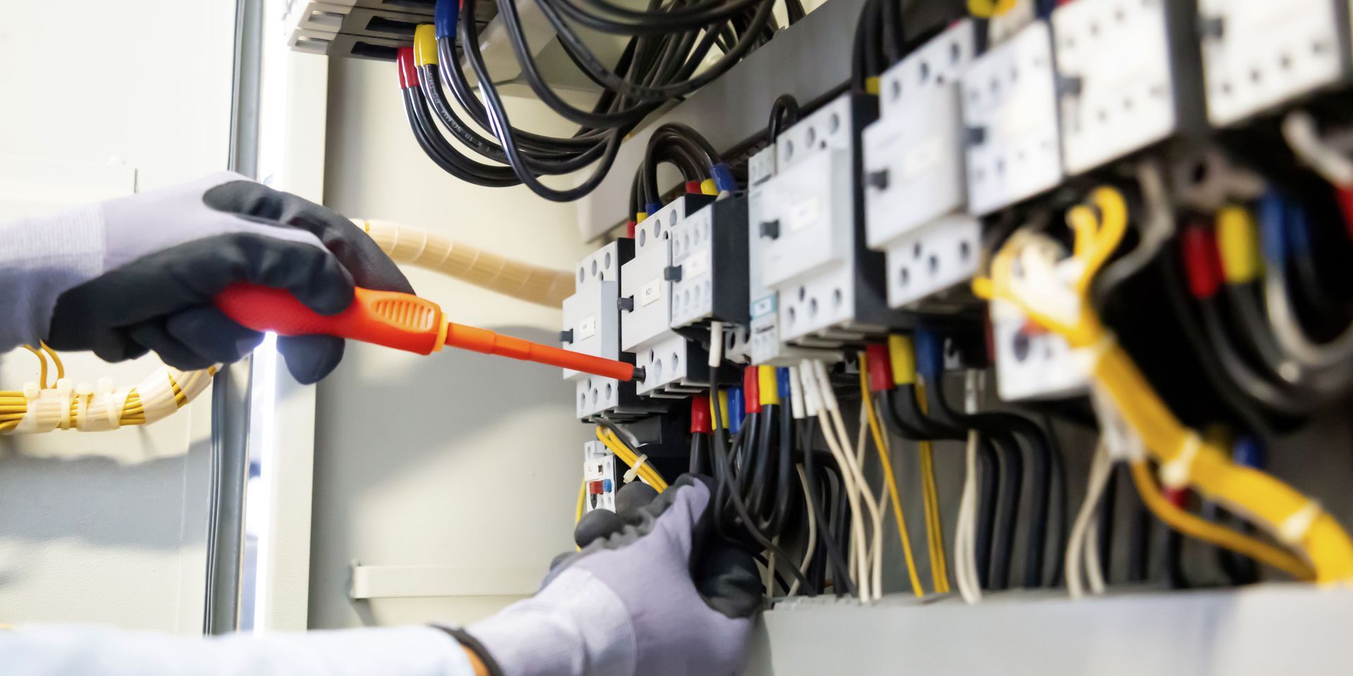An electrician is working on an electrical box with a screwdriver.