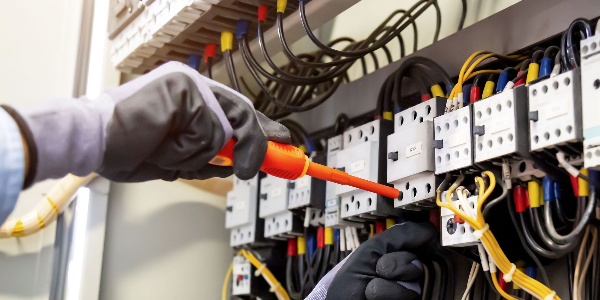 An electrician is working on an electrical panel with a screwdriver.