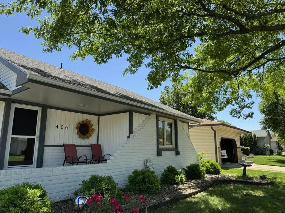 House with white brick and siding, two chairs on the porch, sunflower decoration, and a garage on the right.