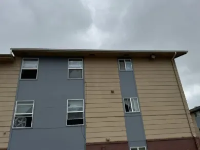 Apartment building with gray and beige siding, windows, and a cloudy sky.