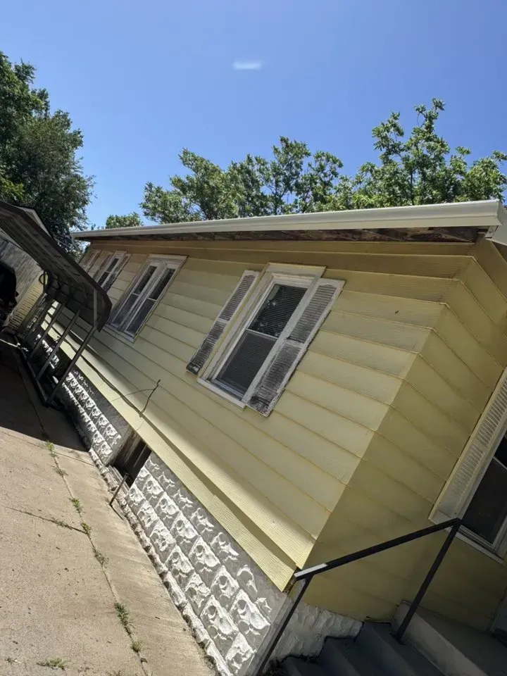 Yellow house with white gutters and shutters, viewed from angled sidewalk on a sunny day.