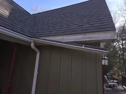 Exterior of a Wichita house with dark roof and green siding. White gutter end is hanging and in need of repair