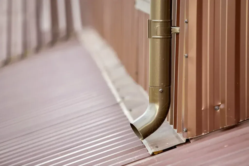 A copper-colored downspout and gutter attached to a corrugated metal wall and roof.