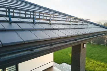 Dark gray tiled roof with ladder-like snow guards, above a black gutter and grassy lawn.