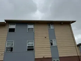 Apartment building with gray and beige siding, windows, and a cloudy sky.