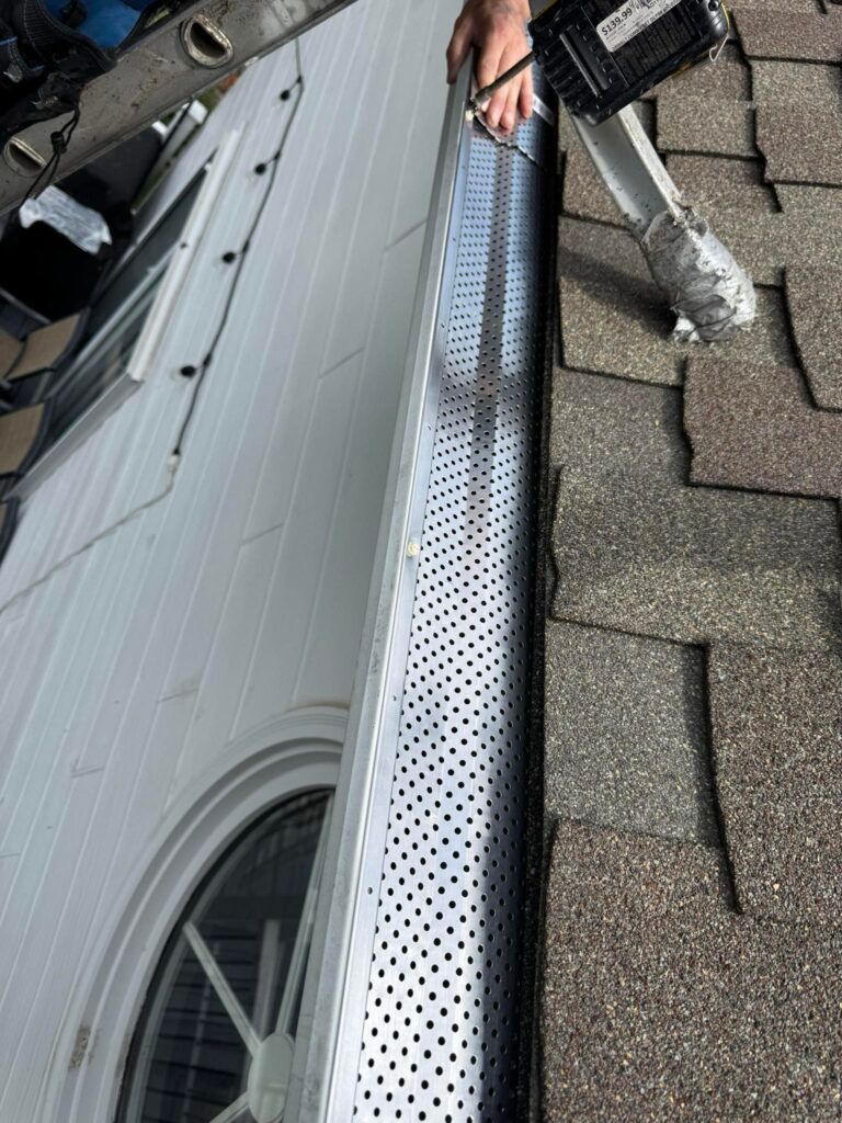 Person installing perforated gutter guard on a roof, next to a white door.
