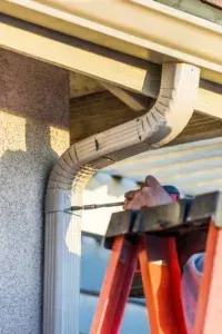 power drill being used to screw in and fasten a downspout to the home