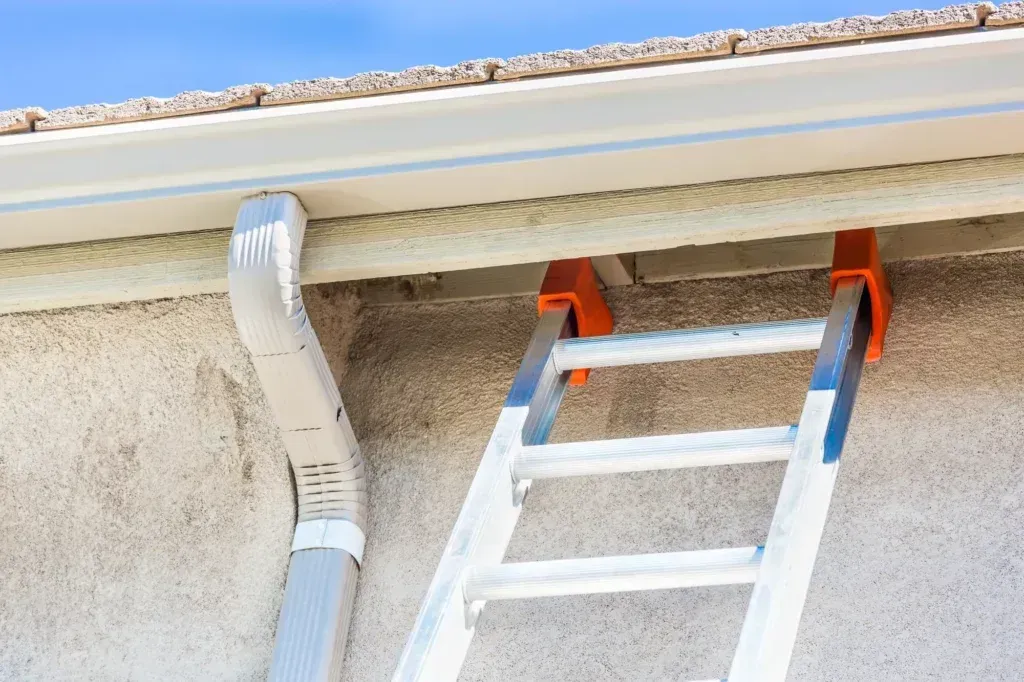 Close up of ladder leaning on side of house just under a seamless gutter system