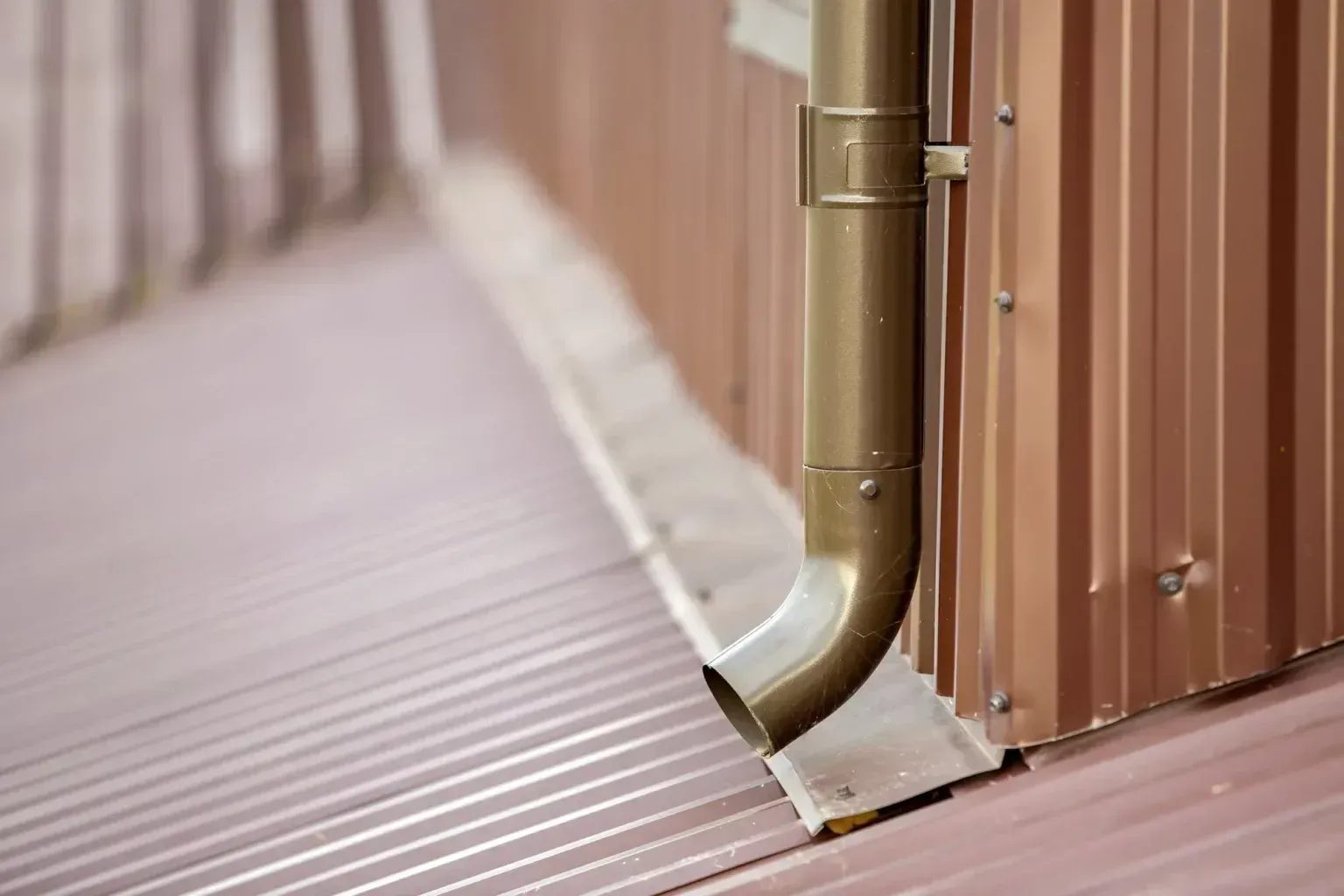 New brown gutter downspout pipe along a bronze metal siding