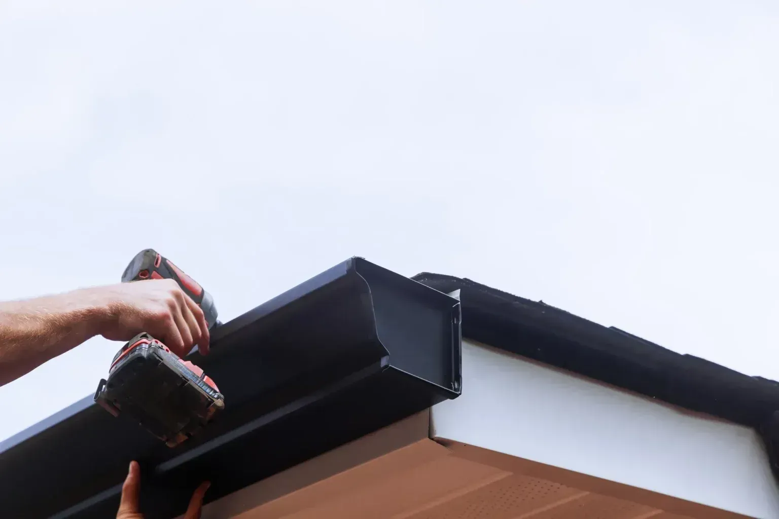 Worker with a power drill over a gutter installing guards in wichita