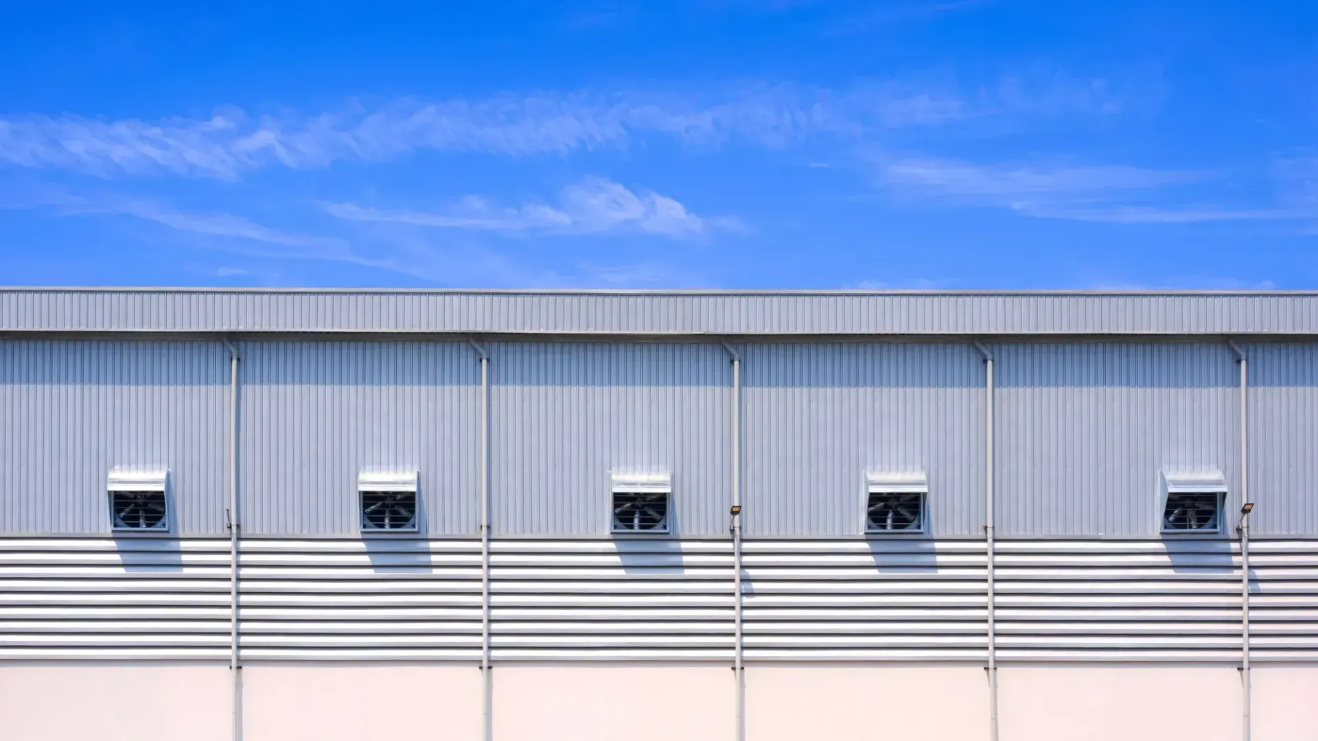 Factory building with vent fans and louver on aluminum steel wall with white downspouts against a blue sky