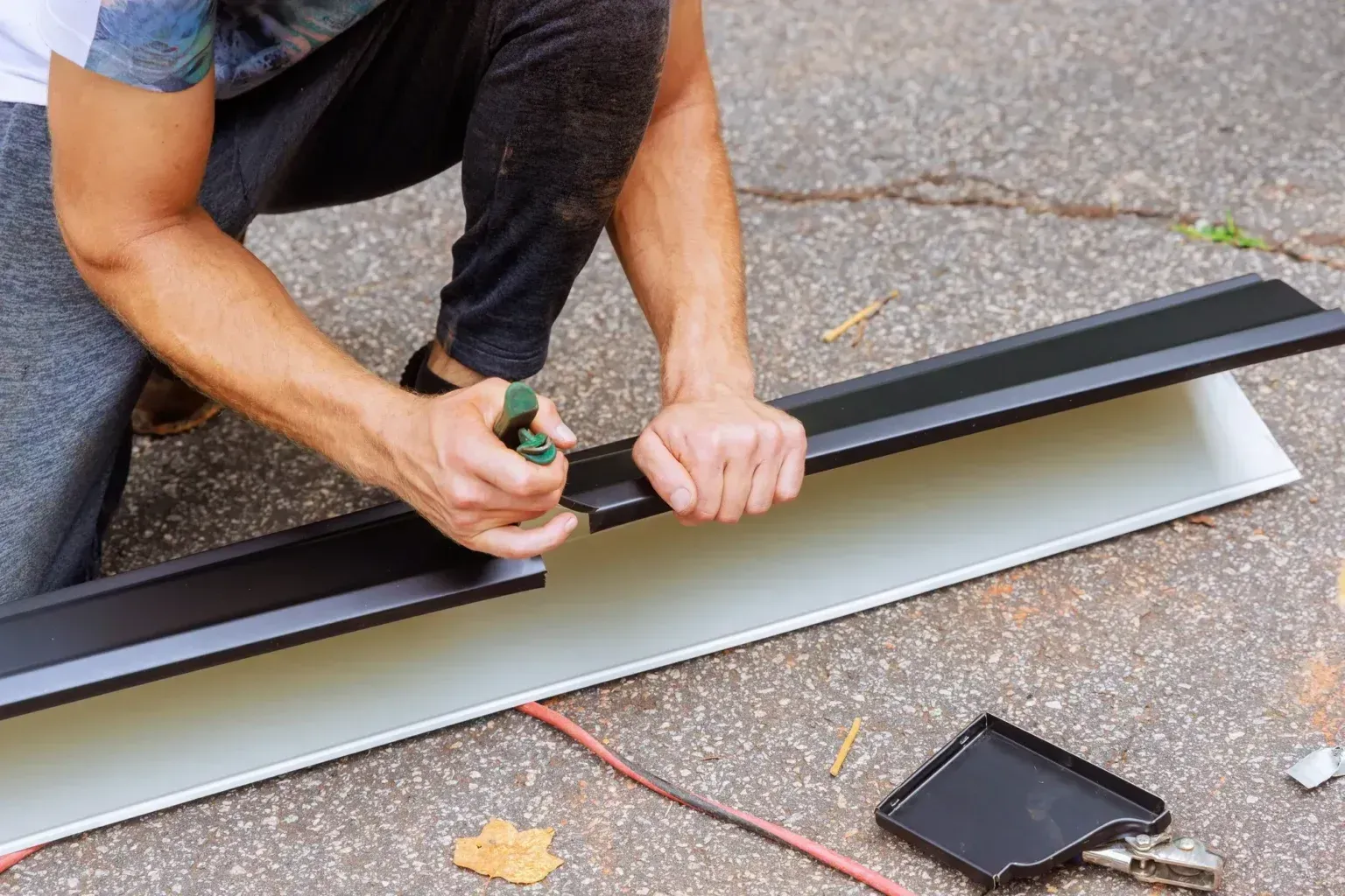 Worker cutting and sizing aluminum rain gutters with shears