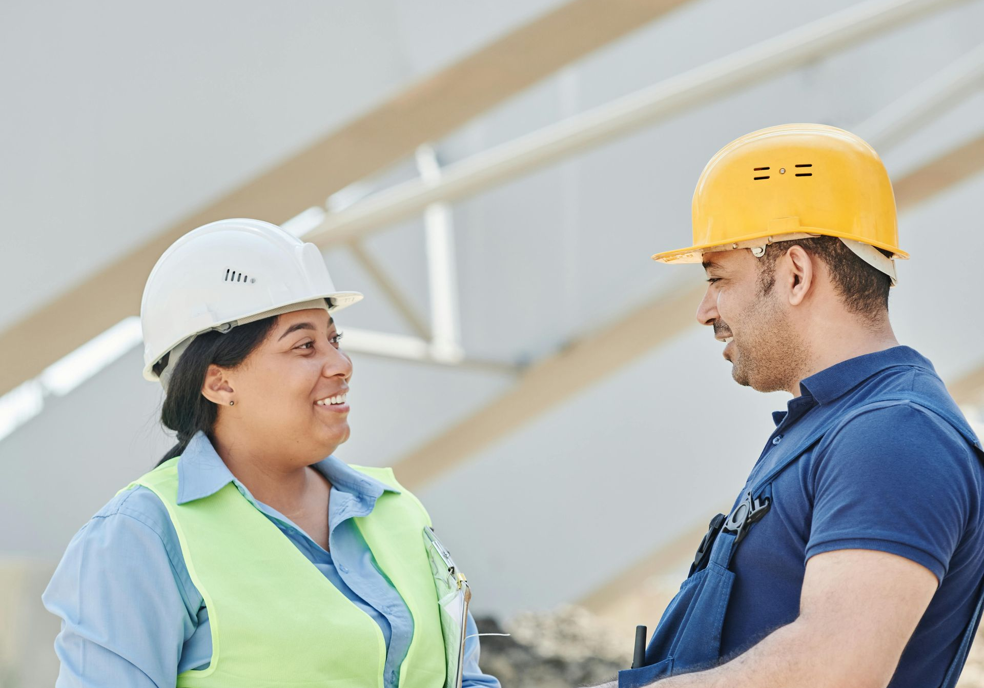 Woman and man construction workers in hard hats smiling, talking on a building site.