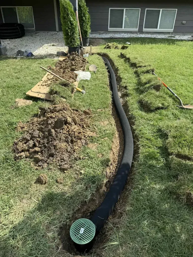 tan downspout off the side of a house leading into a white underground drain