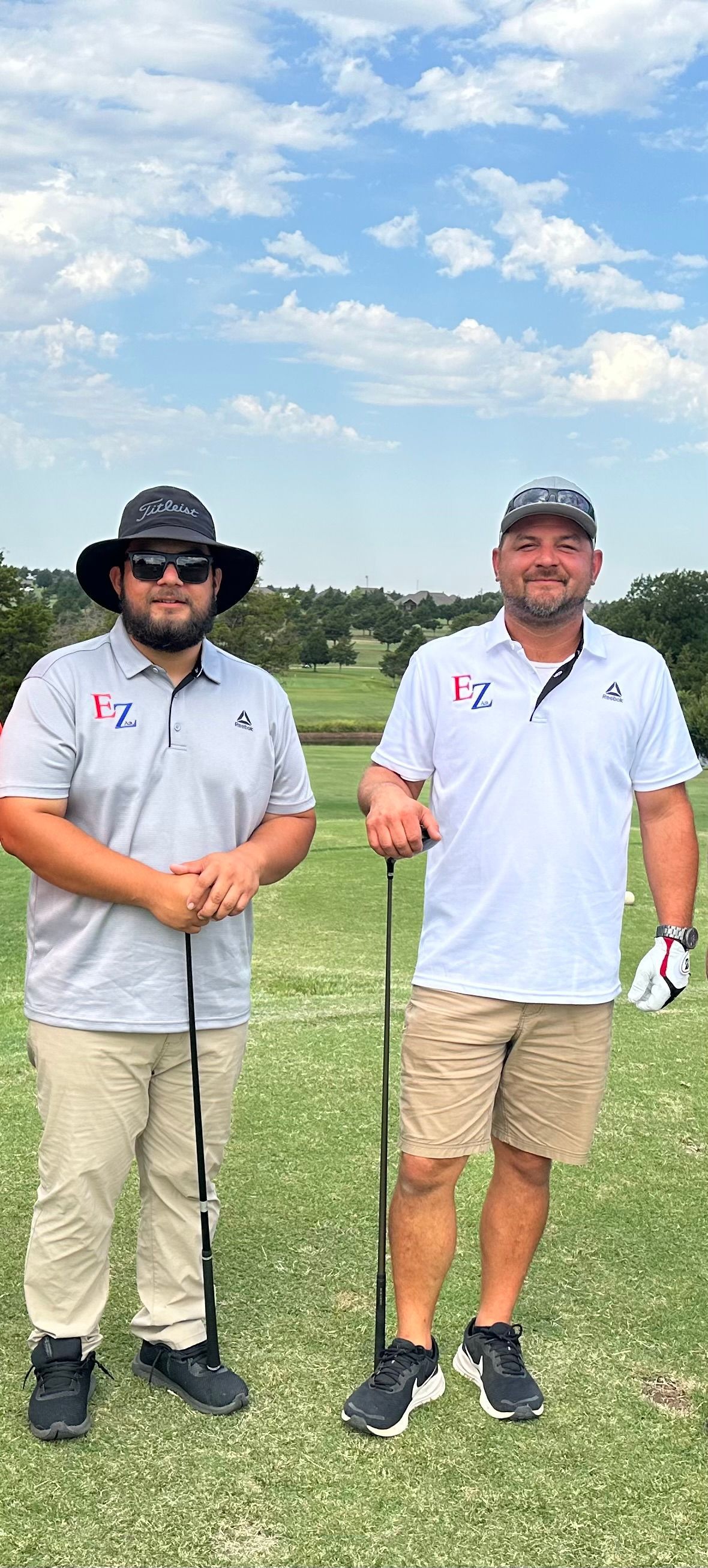 Two men are standing next to each other on a golf course holding golf clubs.