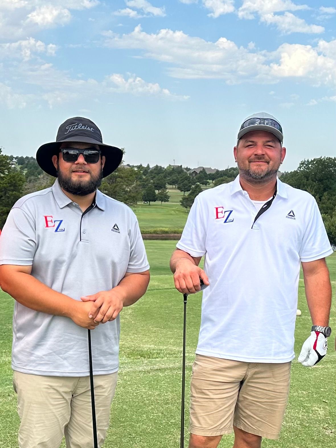 Two men are standing next to each other on a golf course holding golf clubs.