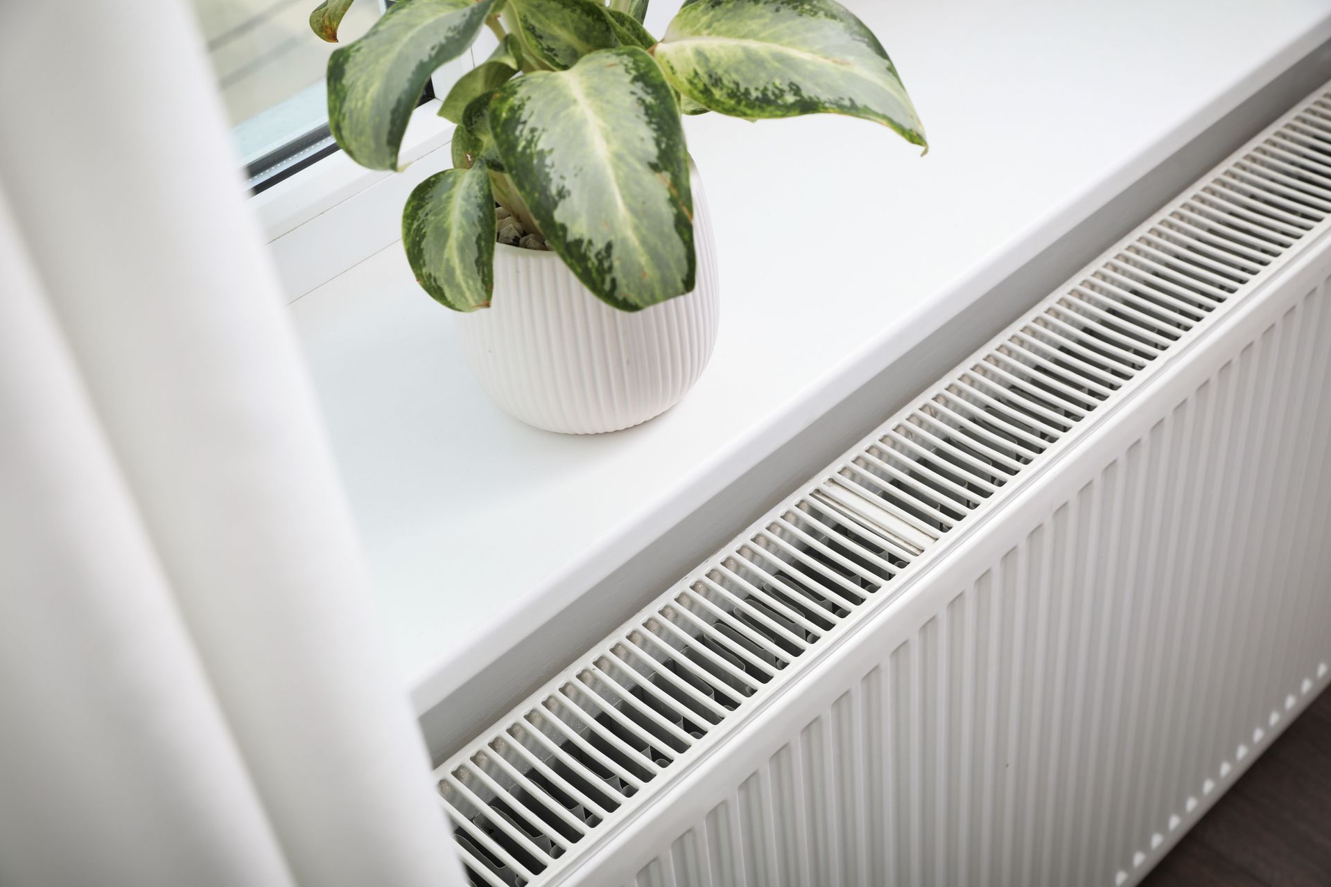 A man is kneeling down in front of a heater while holding a multimeter.
