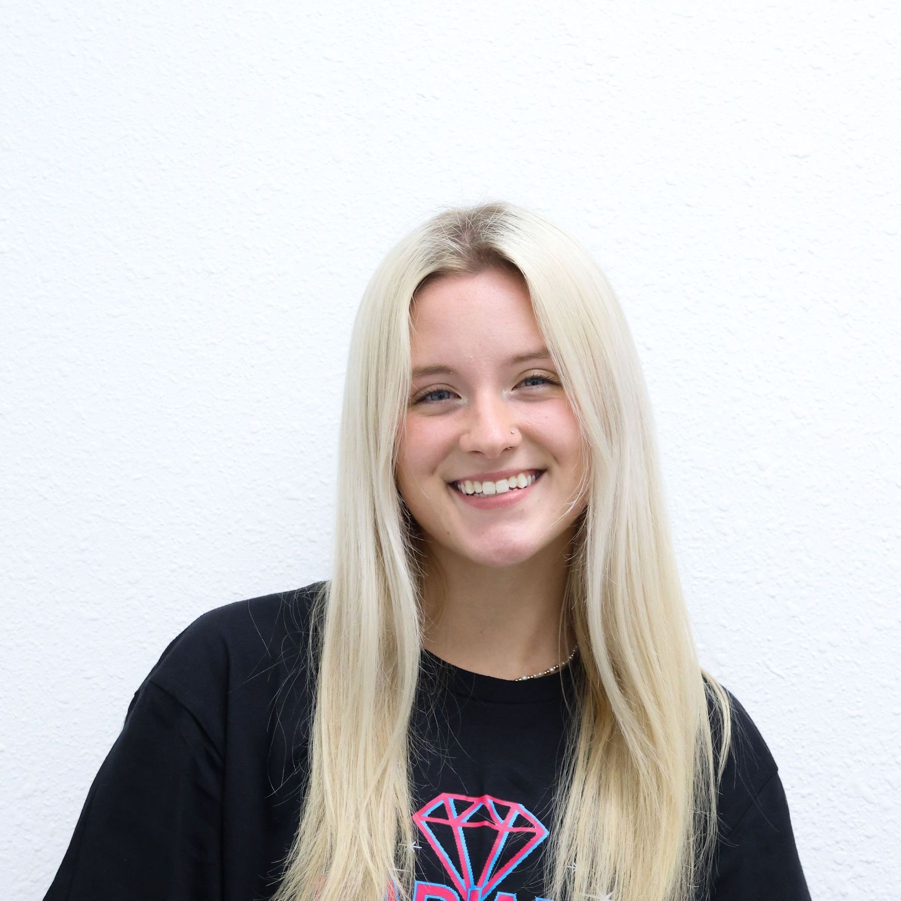 A woman in a purple jacket is smiling with her arms crossed