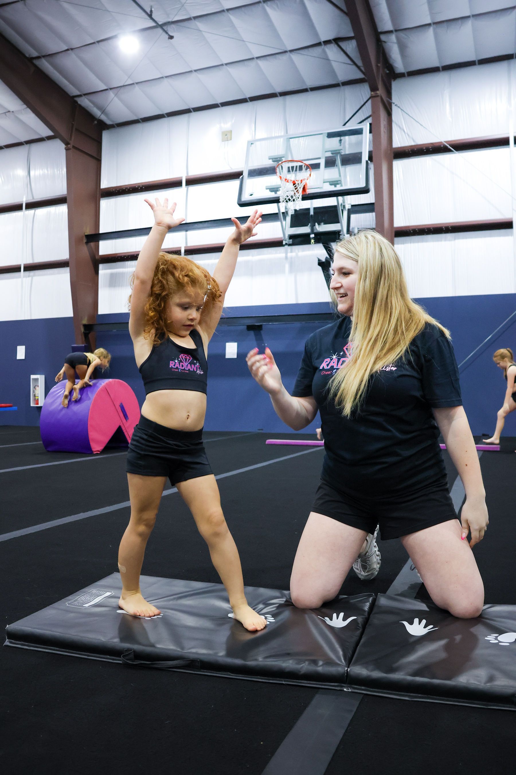 A little girl in a cheerleader outfit is holding purple pom poms