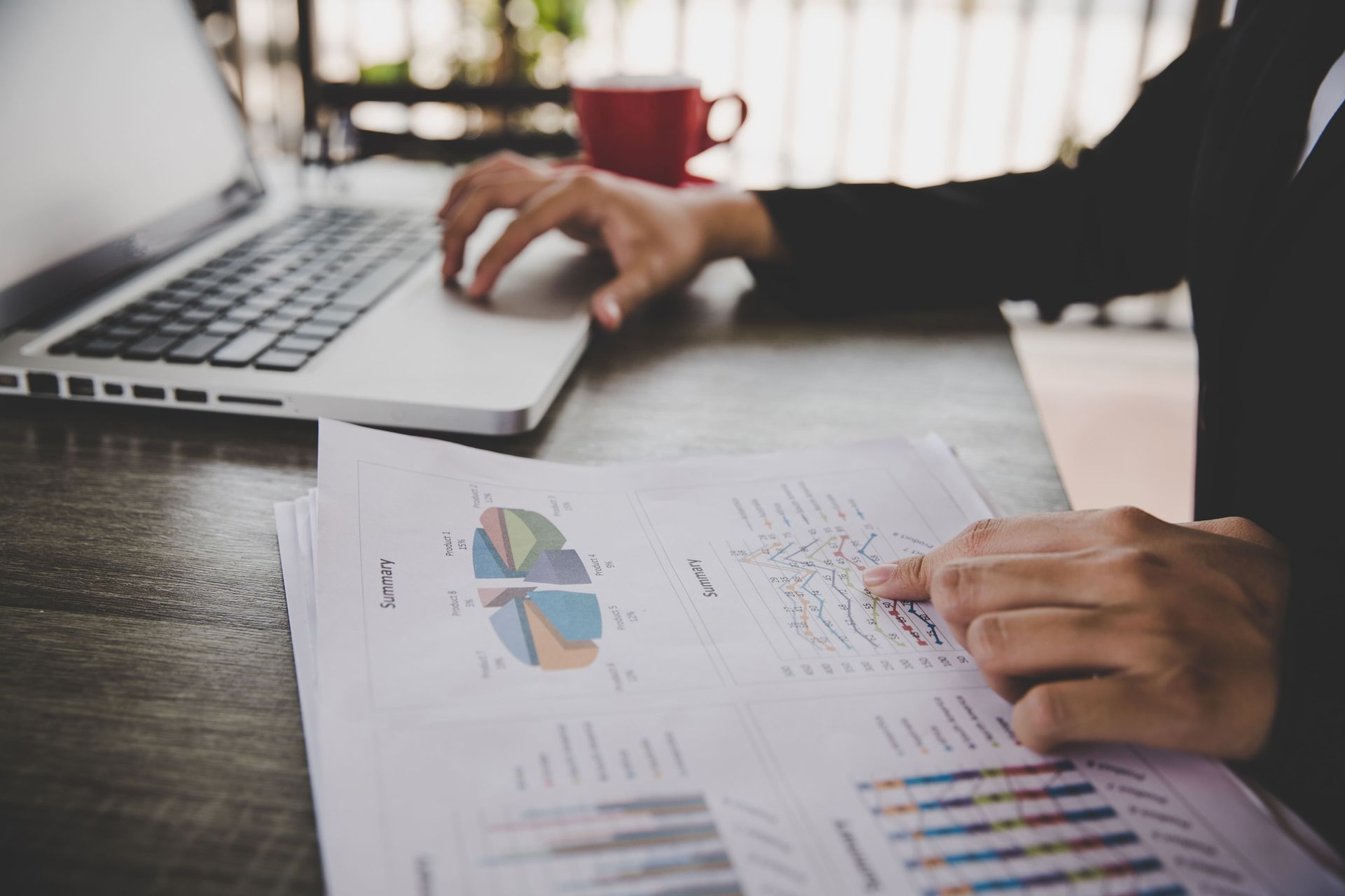 Pessoa de terno aponta para gráficos financeiros enquanto usa laptop.