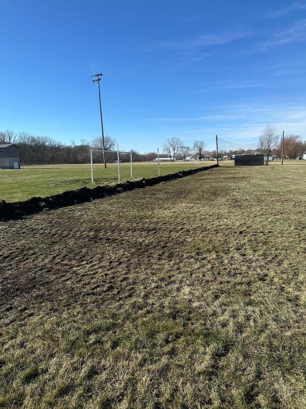 A large grassy field with a fence surrounding it on a sunny day.