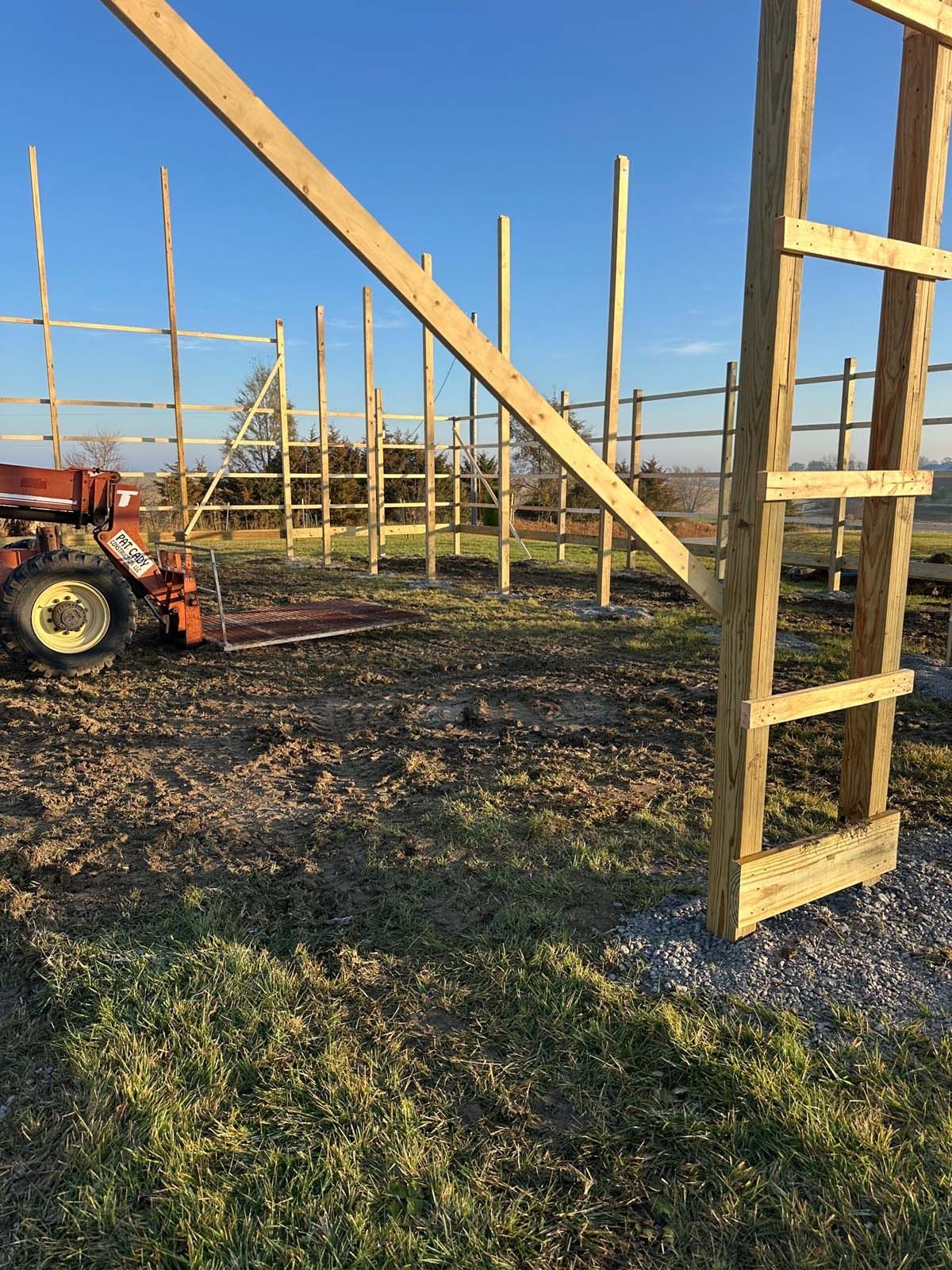 A wooden structure is being built in a field with a tractor in the background.