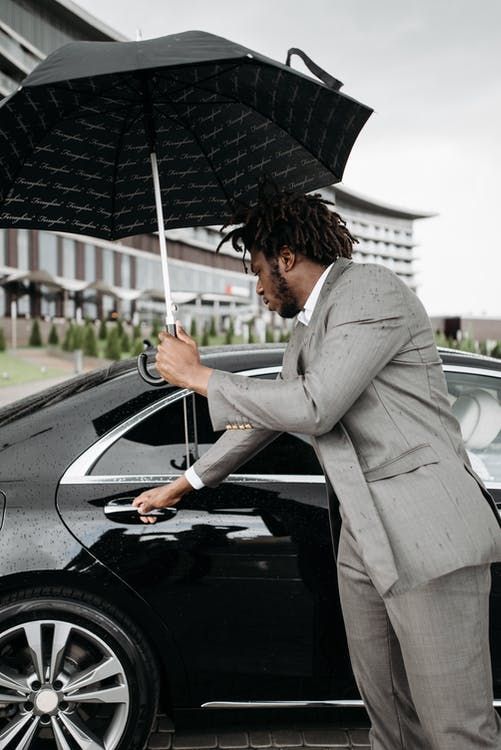 A man in a suit is opening the door of a car while holding an umbrella.
