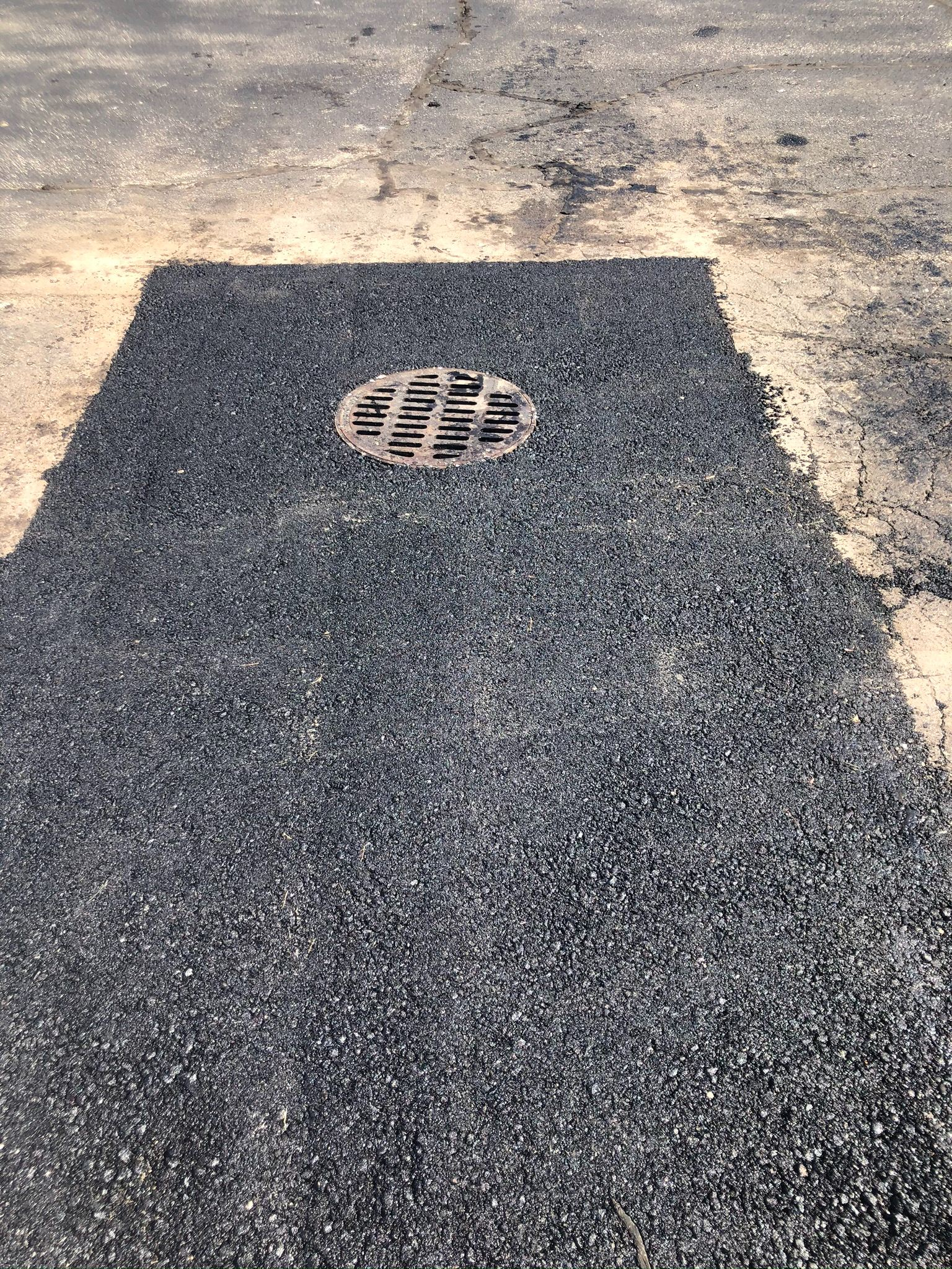 A freshly paved asphalt driveway leading toward a house, flanked by a grassy lawn on one side and a field on the other.