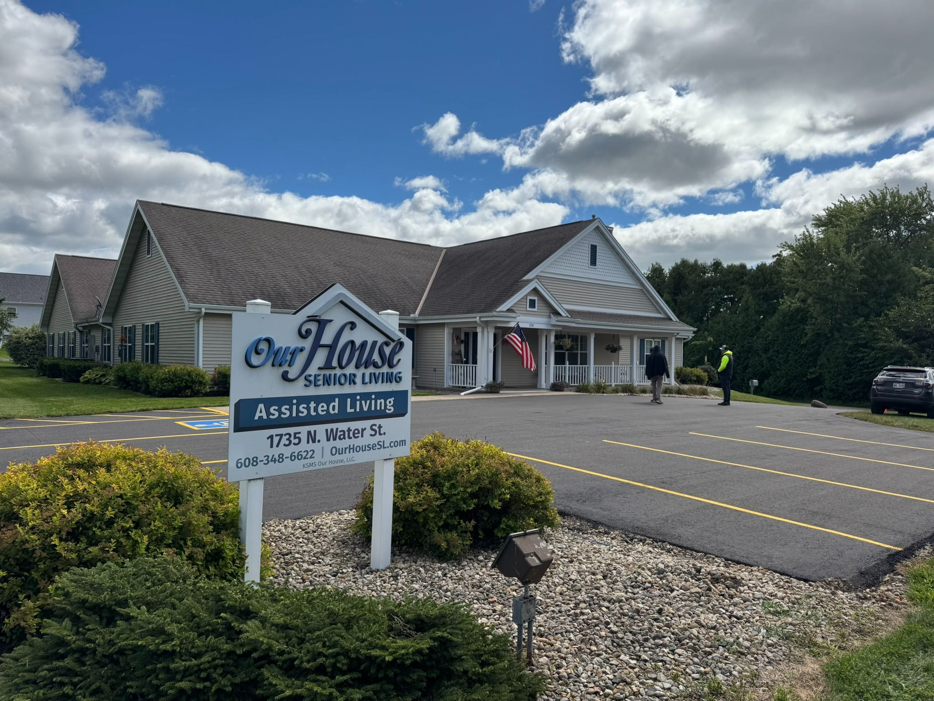 A construction crew uses a dump truck and paving equipment to lay new asphalt outside a commercial building.