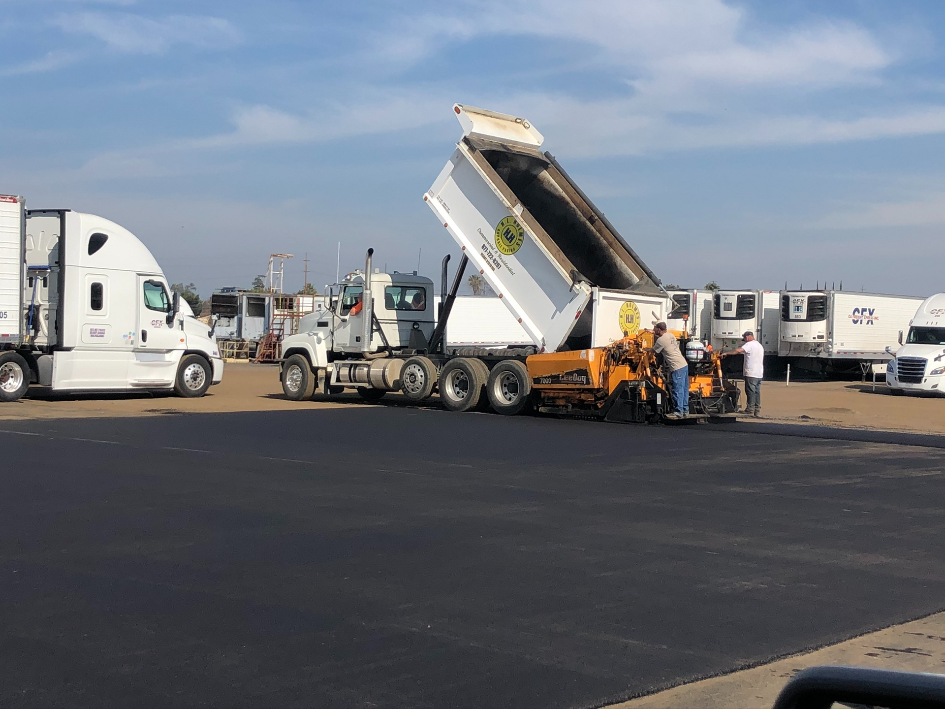 A tan log-style building with a two-car garage opening onto a fresh, dark asphalt driveway on a sunny day.