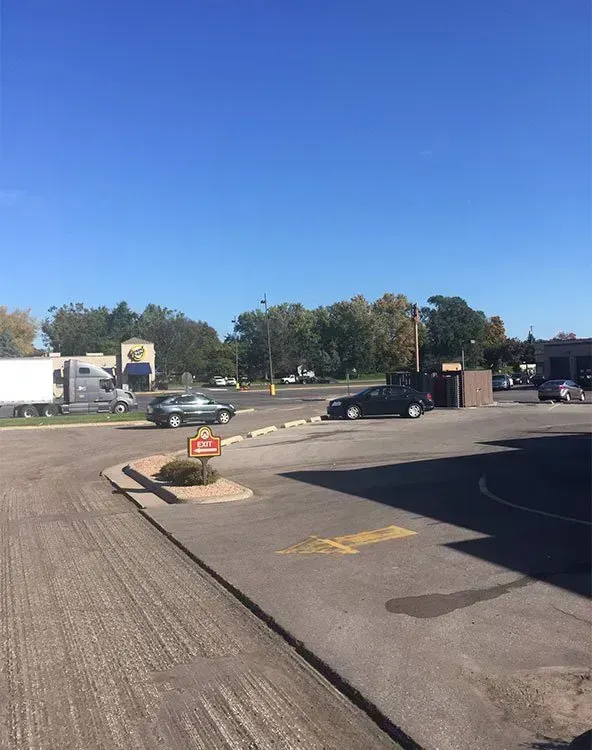 A parking lot on a sunny day with cars and a semi-truck visible in the background.