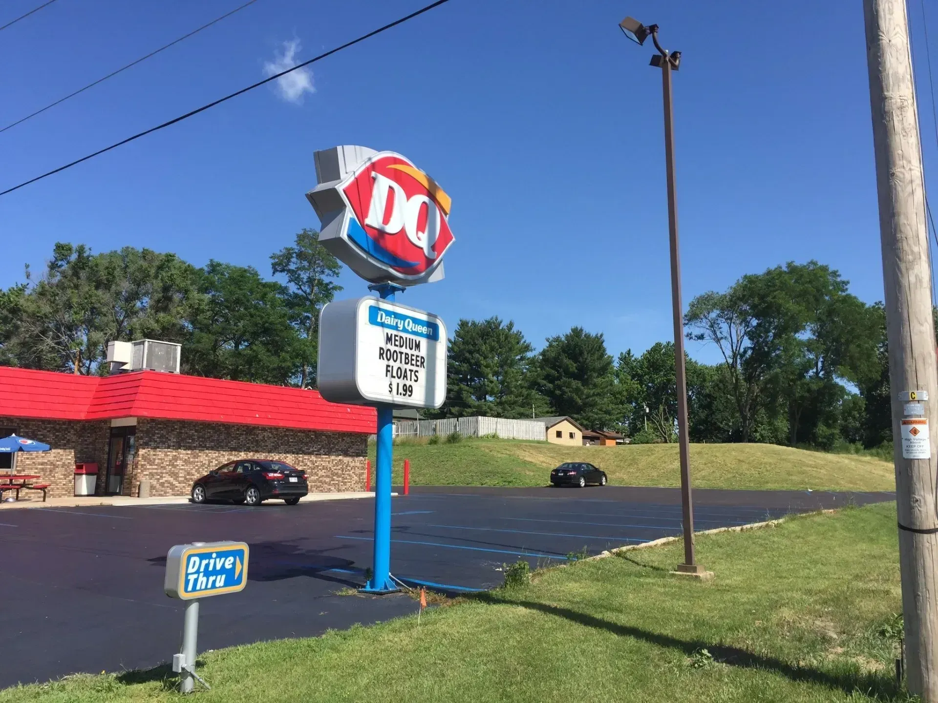 A Dairy Queen restaurant with a red roof, a parking lot, a branded sign, and a drive-thru sign under a clear blue sky.