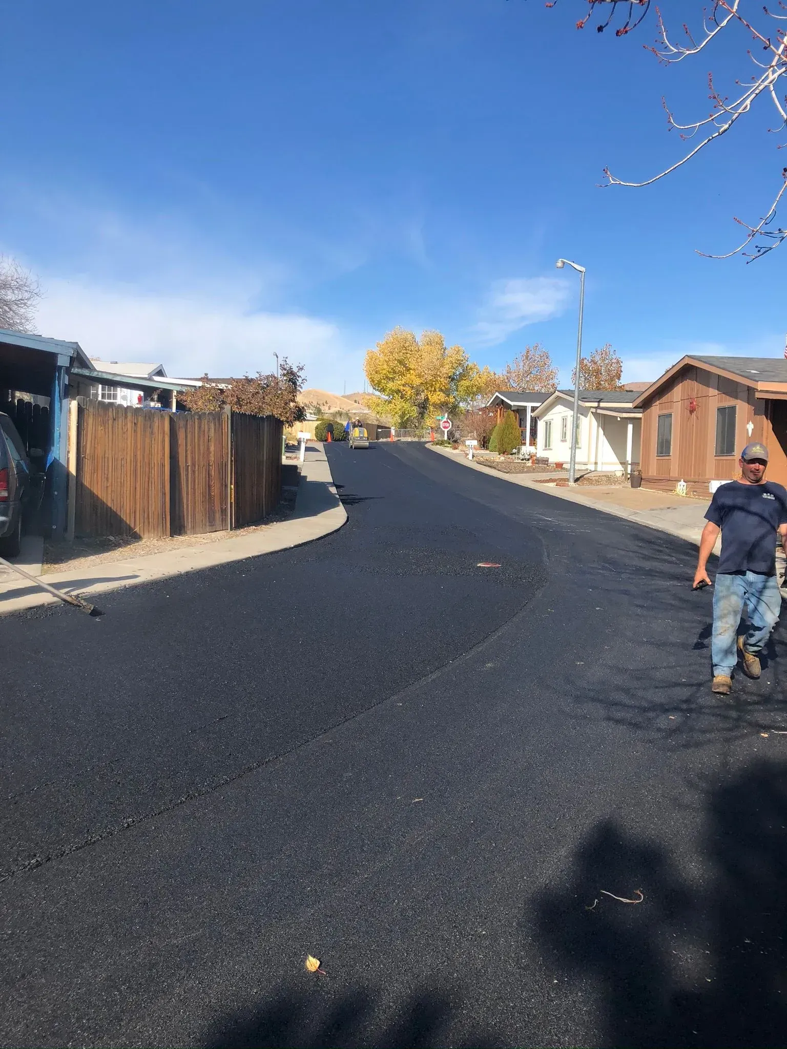 A worker stands on a freshly paved black asphalt road in a residential area on a sunny day.