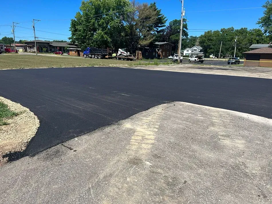 A contrast between freshly laid dark black asphalt and an older, textured gray gravel surface in an outdoor parking lot.