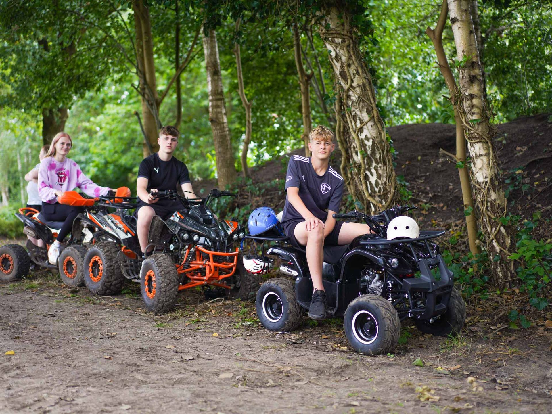 Drei Personen auf Quads auf einem Feldweg in einem Waldgebiet