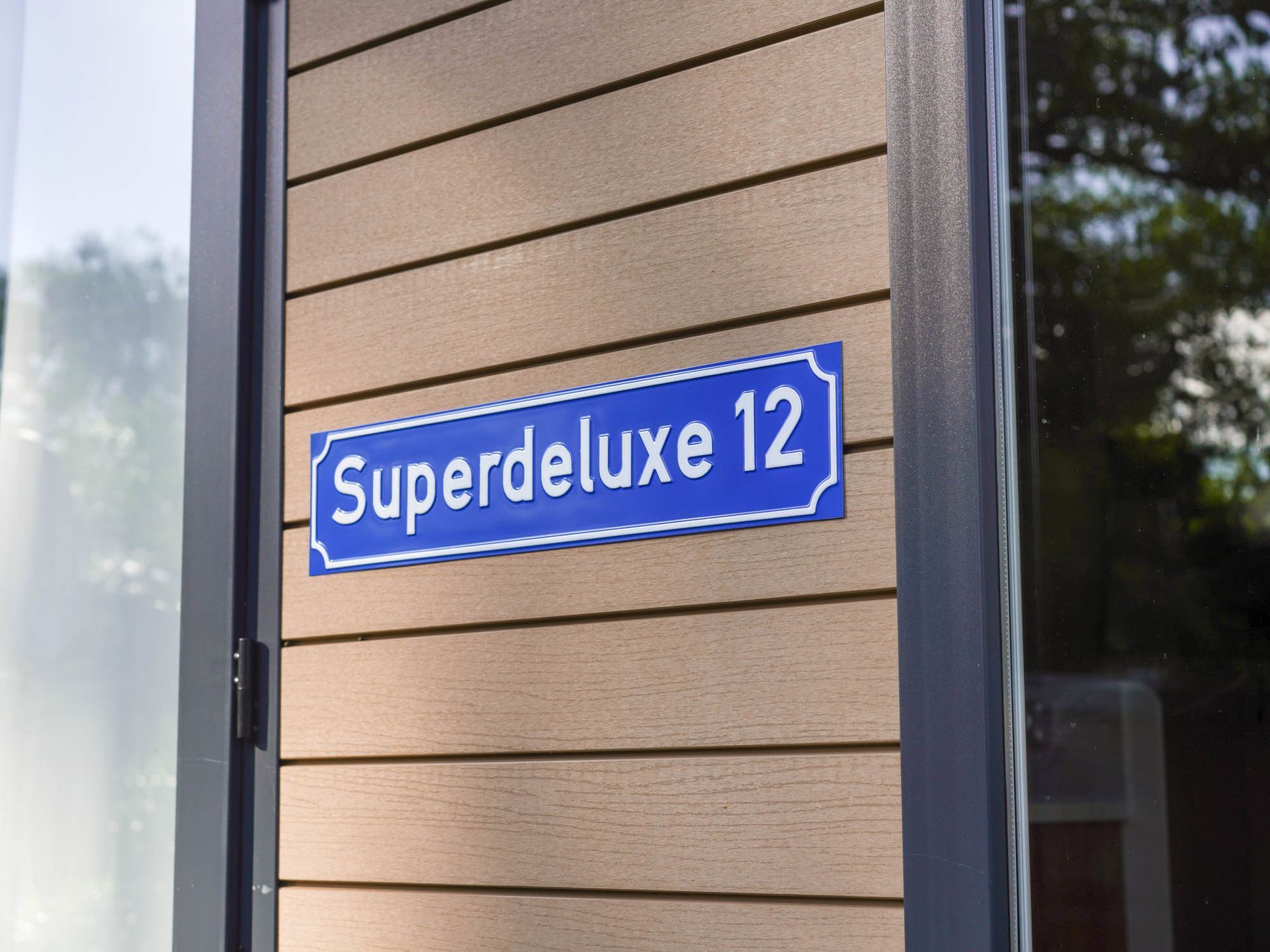Blaues Schild an einem Gebäude mit „Superdeluxe 12“ in weißer Schrift.