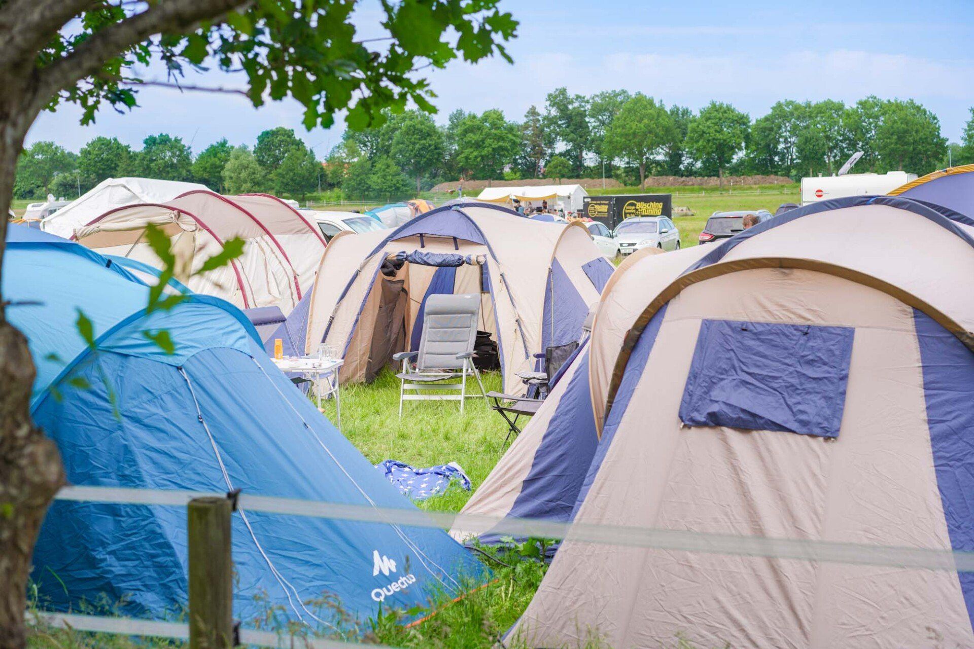 Campingzelte auf einer Wiese, in einem Zelt ist an einem sonnigen Tag ein Stuhl zu sehen.