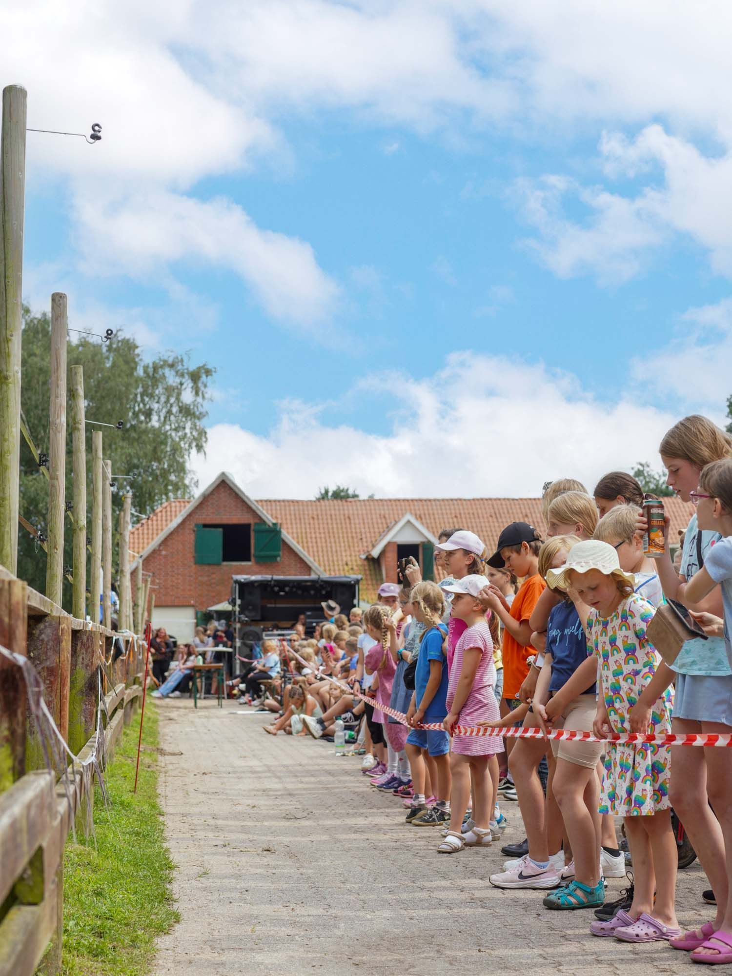 Kinder beobachten eine Veranstaltung im Freien, stehen hinter einer Absperrung
