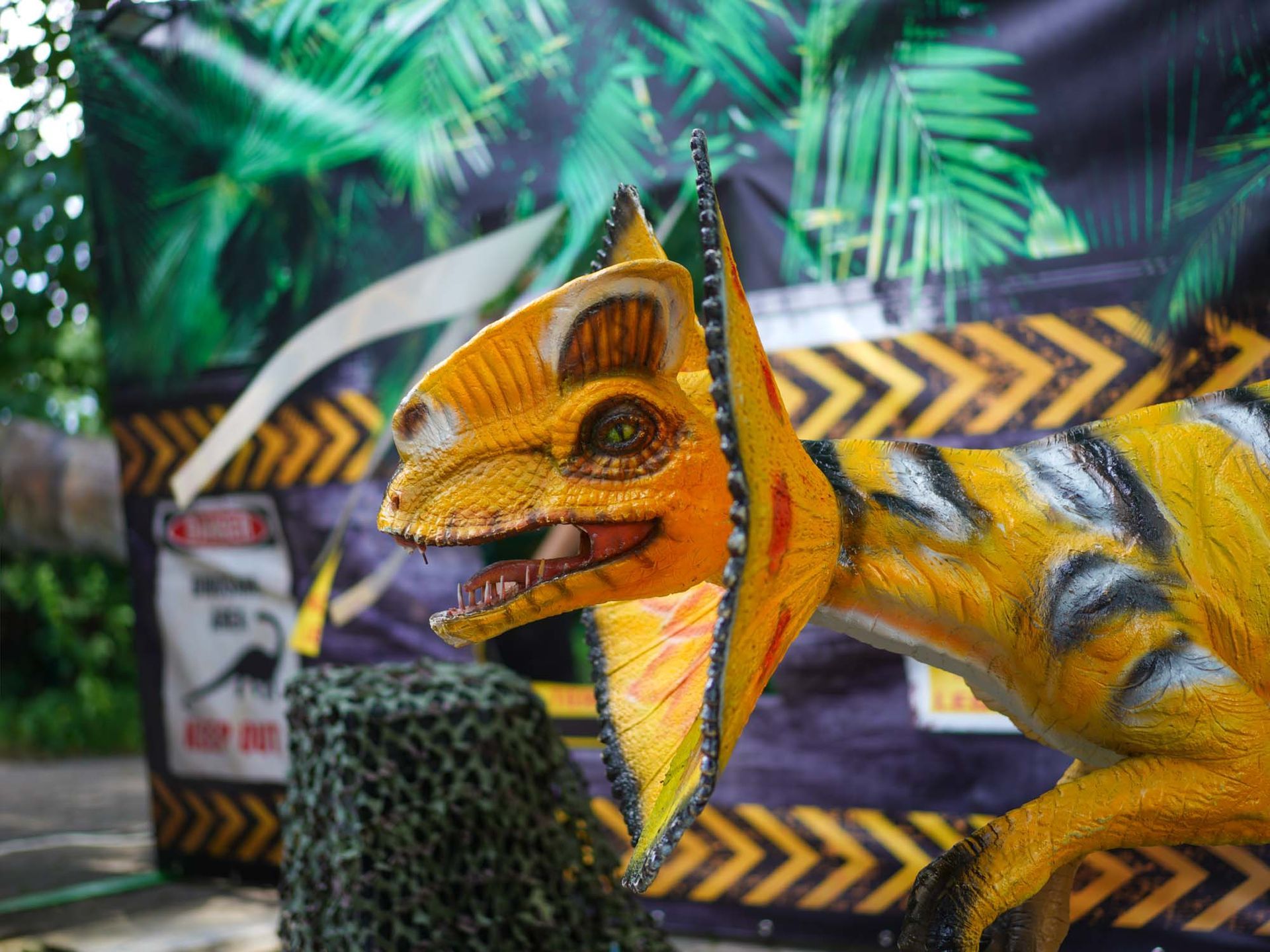 Gelbes Dinosauriermodell mit Rüsche vor dschungelartigen Dekorationen.