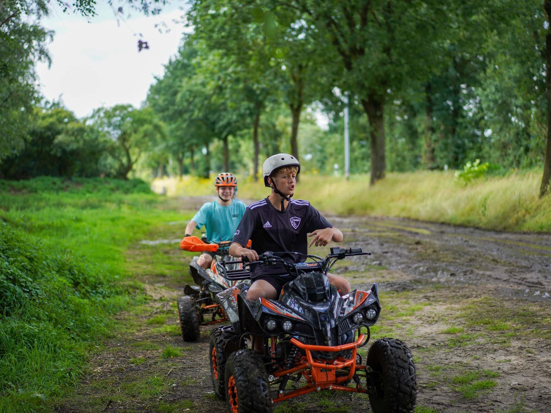 Zwei Personen fahren mit einem Quad auf einem Feldweg durch einen Wald.