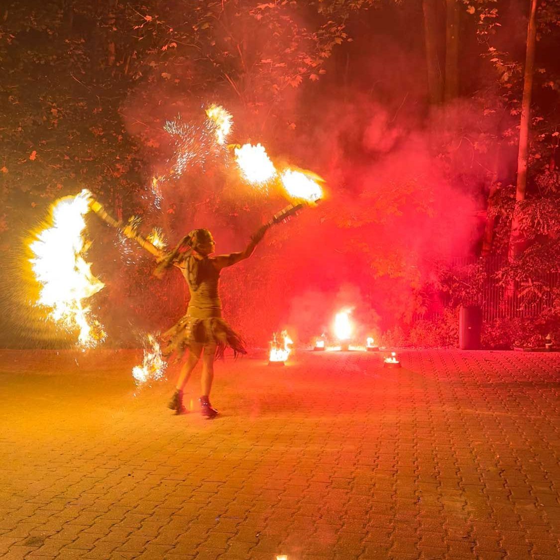 Frau in einem gelben Kleid jongliert nachts draußen mit brennenden Fackeln.