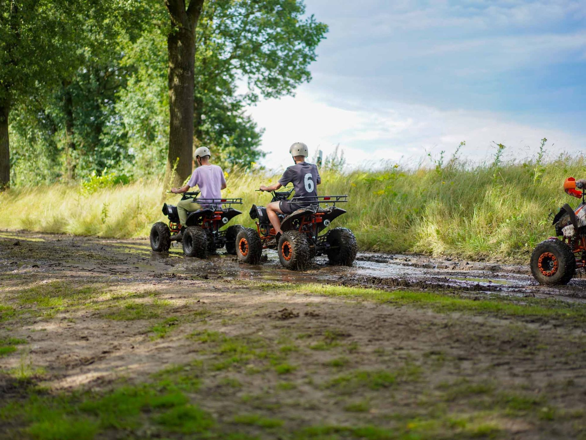Zwei Kinder fahren mit Geländefahrzeugen auf einem schlammigen Feldweg.