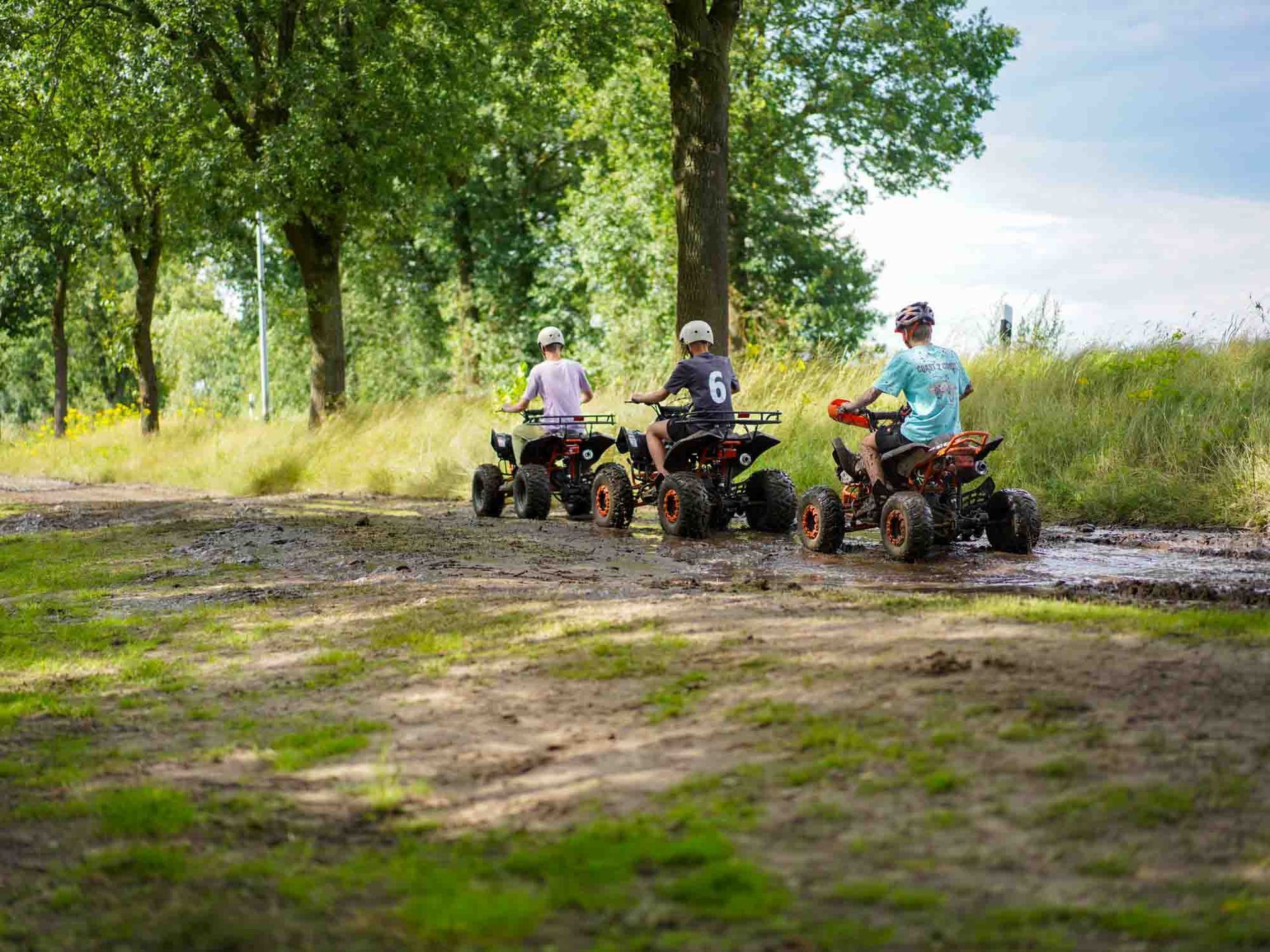Drei Kinder fahren auf Quads auf einem schlammigen Feldweg